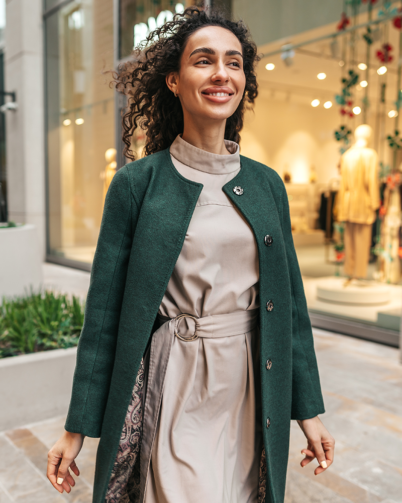 Modelo paseando por la calle con vestido beig y abrigo verde musgo.